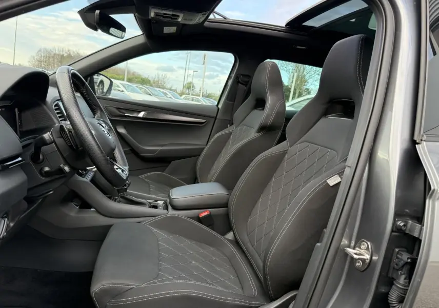 Intérieur avant du Skoda Karoq gris graphite, sièges sport noirs avec surpiqûres blanches et toit ouvrant panoramique en verre.