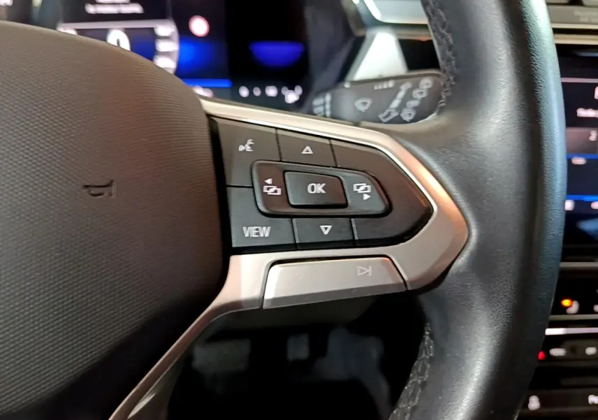 Gros plan sur les commandes du volant cuir noir du Volkswagen Touran gris foncé 2023, avec affichage digital en arrière-plan.