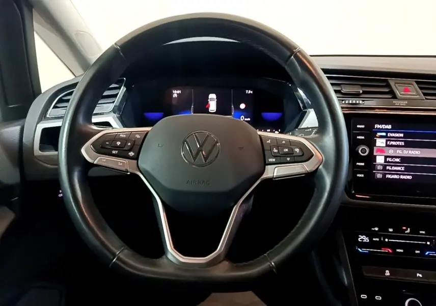Vue intérieure centrée sur le volant cuir noir du Volkswagen Touran 2023 avec tableau de bord digital et écran tactile.