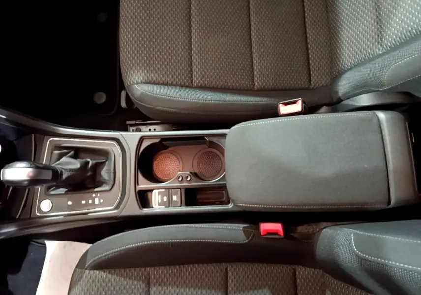 Vue plongeante sur la console centrale du Volkswagen Touran gris foncé, avec levier de vitesses automatique et accoudoir rembourré.