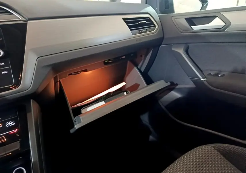 Intérieur du Volkswagen Touran 2023 gris foncé, vue côté passager avec boîte à gants ouverte et éclairage intérieur.