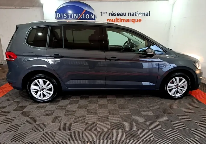 Profil droit d'un Volkswagen Touran gris foncé 2023 garé en intérieur avec jantes alliage et vitres teintées.