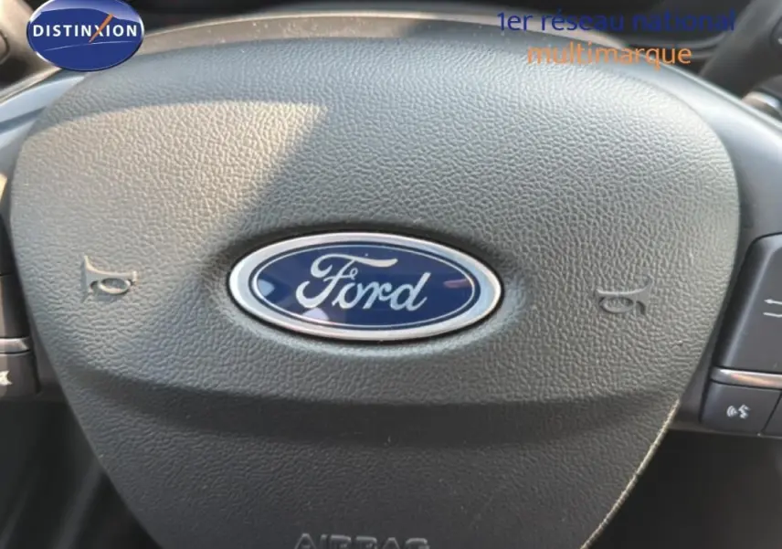 Gros plan sur le volant noir avec logo Ford bleu au centre d'une Ford Focus SW 2022, finition Titanium X Business.