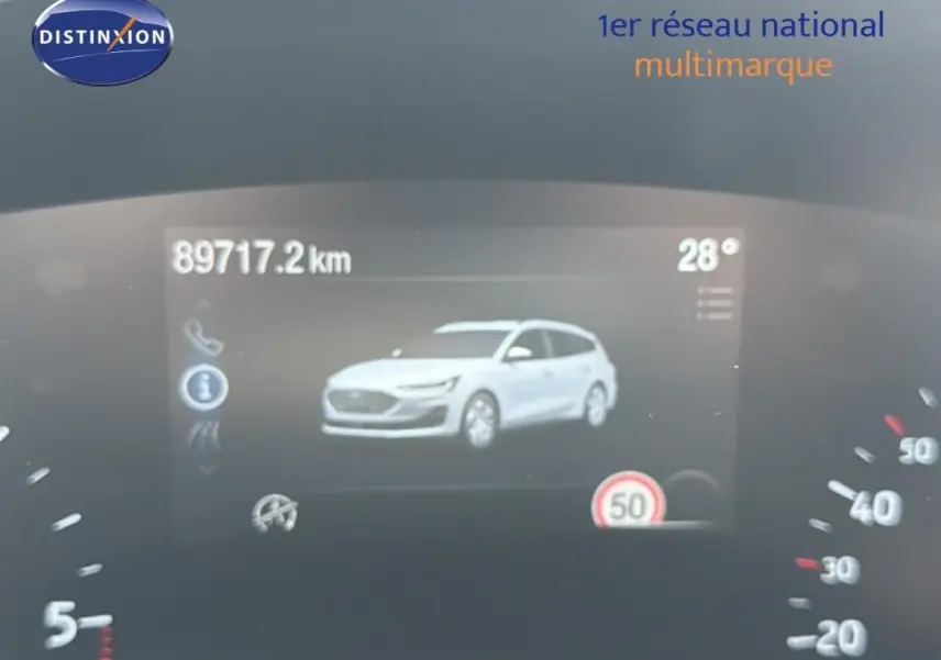 Affichage numérique du tableau de bord montrant une Ford Focus SW blanche en vue 3/4 avant, avec compteur et température.