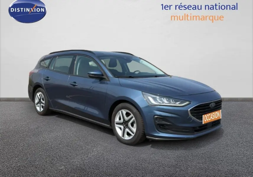Ford Focus SW bleu foncé vue 3/4 avant droit, avec barres de toit et jantes classiques 16 pouces visibles.