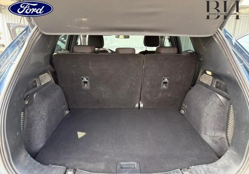 Coffre ouvert du Ford Kuga bleu, vue arrière montrant la banquette arrière noire et l'espace de chargement.