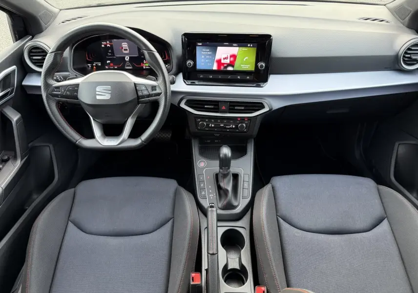 Vue intérieure frontale du tableau de bord et des sièges gris foncé d'une SEAT IBIZA 2024 avec volant multifonction et écran tactile central.