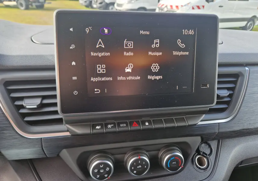 Écran tactile central avec menu multimédia et commandes de climatisation sur tableau de bord du Nissan Primastar gris urbain.