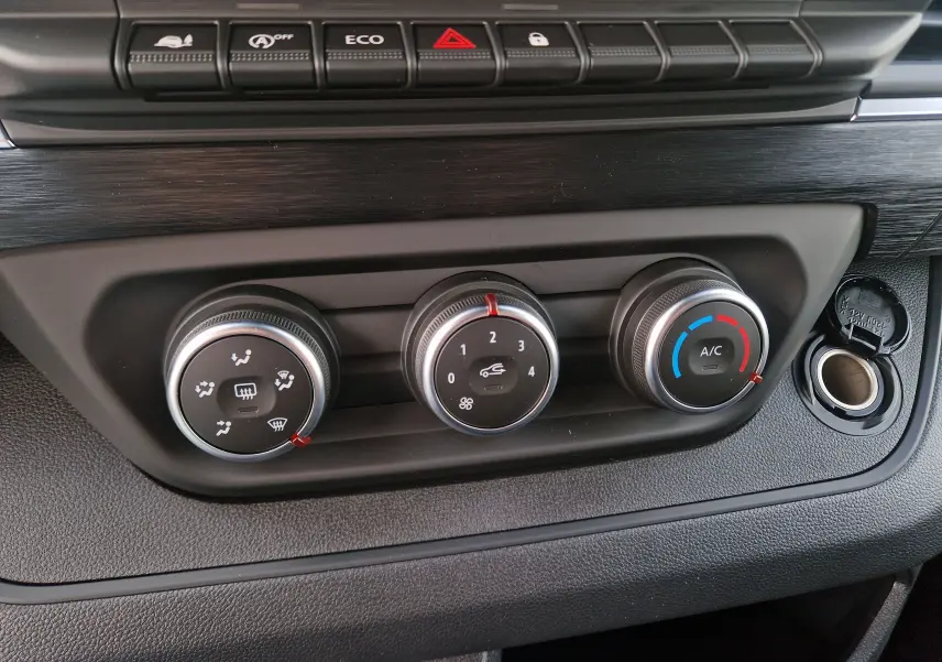 Gros plan sur les commandes de climatisation du Nissan Primastar 2025, avec boutons rotatifs et prise 12V visible.