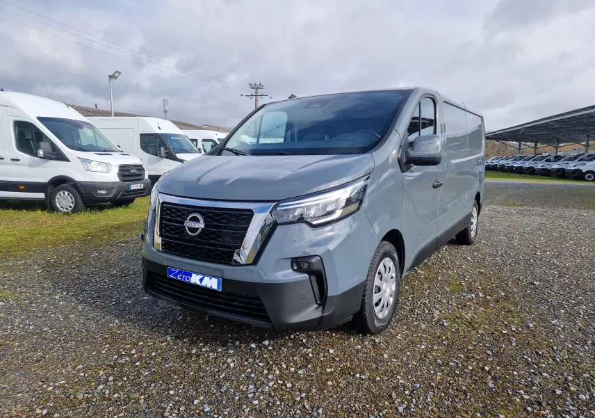 Nissan Primastar gris urbain vu en 3/4 avant droit sur un parking de véhicules utilitaires.