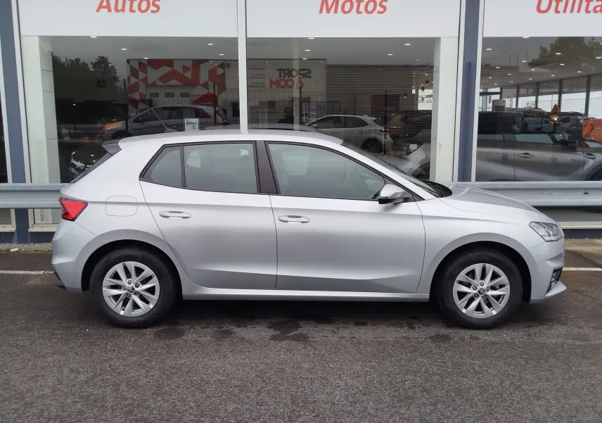 Vue de profil côté gauche d'une Skoda Fabia gris argent métallisé stationnée devant une vitrine de concession.