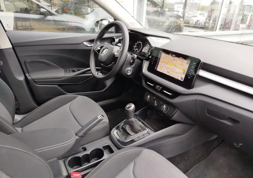 Vue intérieure côté conducteur de la Skoda Fabia 2023, tableau de bord noir avec écran tactile et levier de vitesses manuel.