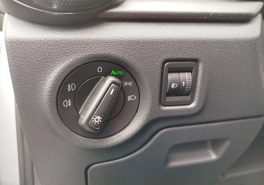 Gros plan sur le bouton de commande des phares avec réglage automatique, intérieur noir texturé de la Skoda Fabia gris argent 2023.