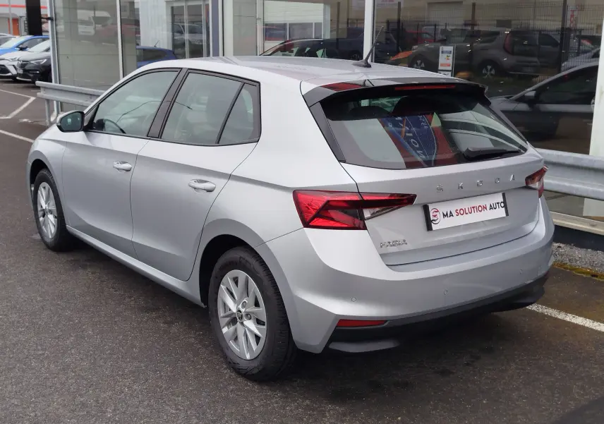 Vue 3/4 arrière droite d'une Skoda Fabia gris argent métallisé garée devant un bâtiment vitré.