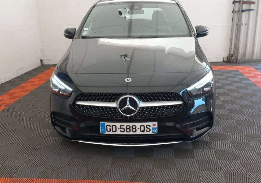 Vue avant d'une Mercedes Classe A Berline A 200 AMG Line noire avec calandre à étoile et phares LED allumés.