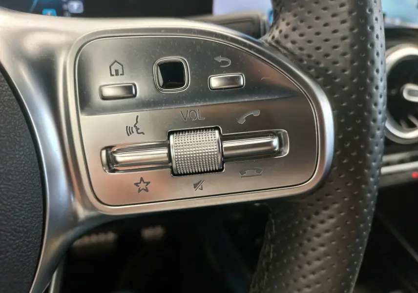 Gros plan sur les commandes argentées du volant en cuir perforé d’une Mercedes Classe A A 200 AMG Line noire.