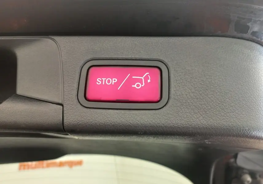 Bouton rouge STOP ouverture/fermeture coffre sur panneau intérieur noir d’une Mercedes Classe A berline noire.