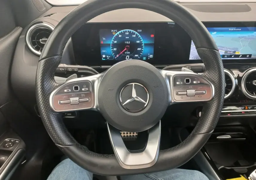 Vue intérieure centrée sur le volant cuir perforé de la Mercedes Classe A A 200 AMG Line avec tableau de bord numérique et écran tactile.