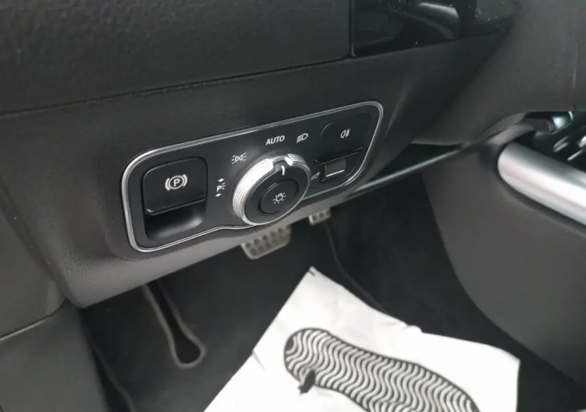 Détail du panneau de commande des phares et frein à main électrique côté conducteur dans une Mercedes Classe A noire.
