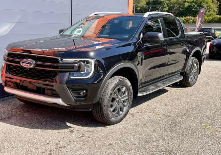 Ford Ranger 2025 noir agate en 3/4 avant droit, avec calandre imposante et jantes alliage foncé Wildtrak Plus.
