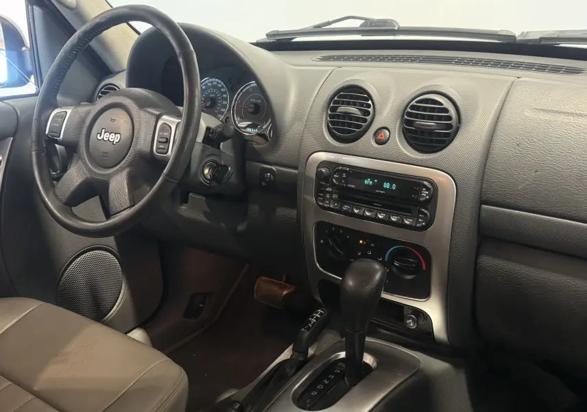 Vue intérieure côté conducteur du Jeep Cherokee 2005 bleu, montrant le volant, tableau de bord et levier de boîte auto.