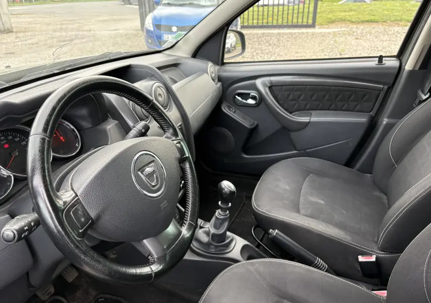 Vue intérieure côté conducteur du Dacia Duster 2014, montrant le volant, la boîte manuelle et les sièges noirs.