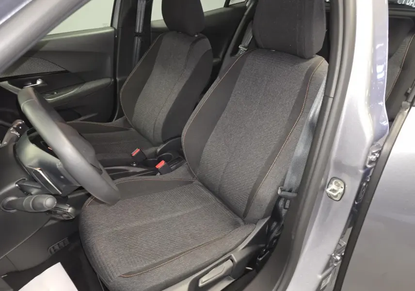 Vue intérieure côté conducteur du Peugeot 2008 gris 2025, sièges tissu gris avec surpiqûres orange et volant compact cuir.