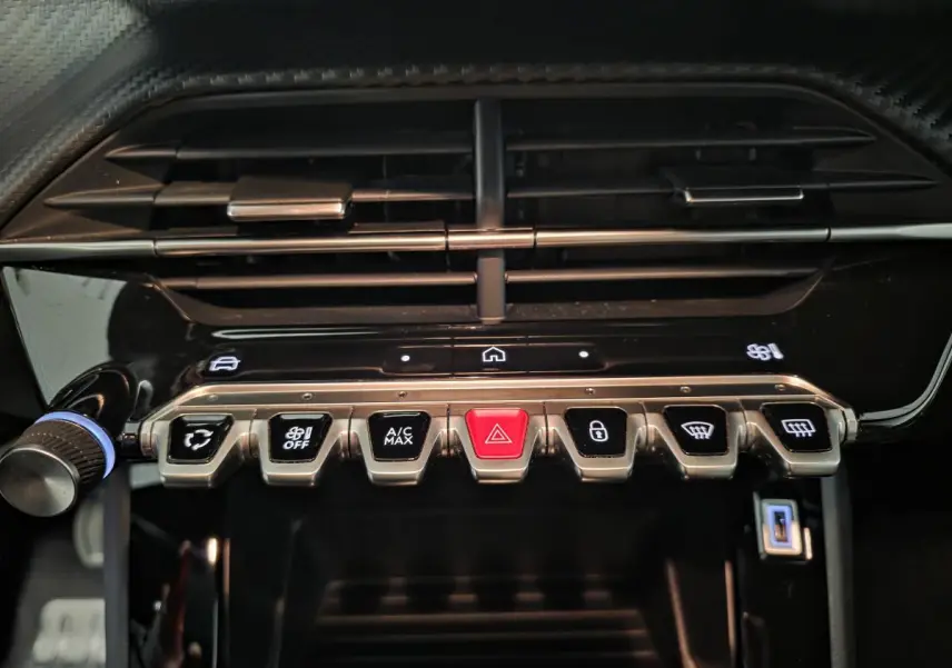 Gros plan sur la rangée de boutons de commande sous la sortie d'air centrale du tableau de bord noir brillant du Peugeot 2008 gris.