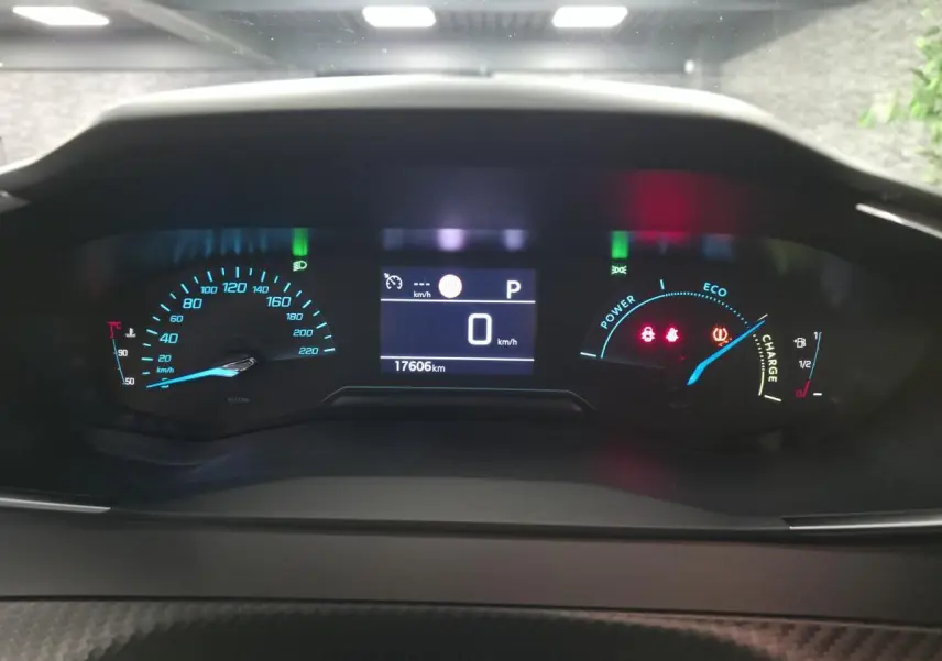 Vue rapprochée du tableau de bord numérique du Peugeot 2008 gris, affichant la vitesse à 0 km/h et l'autonomie hybride.