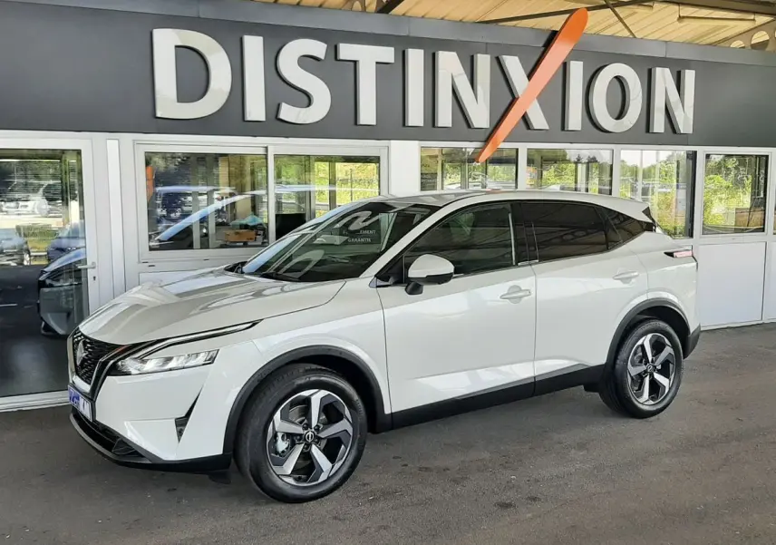 Nissan Qashqai blanc lunaire en 3/4 avant droit, avec jantes bi-ton et vitres teintées sous un auvent Distinxion.
