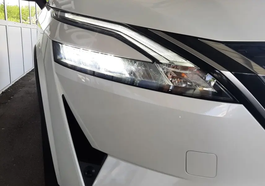 Gros plan sur le phare avant gauche allumé du Nissan Qashqai blanc lunaire 2022, soulignant son design moderne.