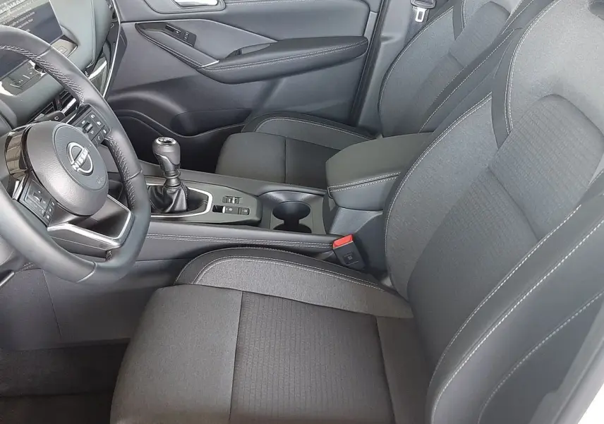 Vue intérieure côté conducteur du Nissan Qashqai 2022 avec sièges en tissu gris et levier de vitesses manuel.