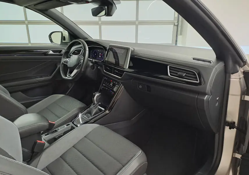 Intérieur côté conducteur du Volkswagen T-Roc Cabriolet gris ivoire, tableau de bord moderne avec écran tactile central.