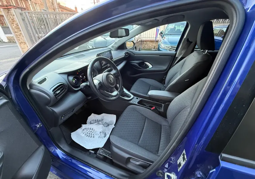 Intérieur de la Toyota Yaris Hybride bleu métal, vue côté gauche avec sièges tissu gris et tableau de bord moderne.