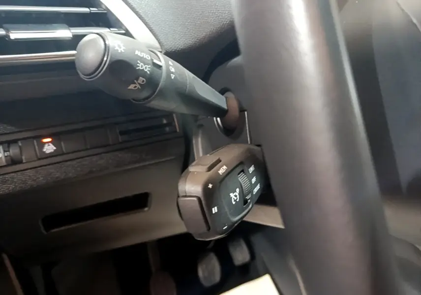 Gros plan sur la commande de régulateur de vitesse et le commodo d’éclairage dans l’habitacle noir du Peugeot 3008 2022.