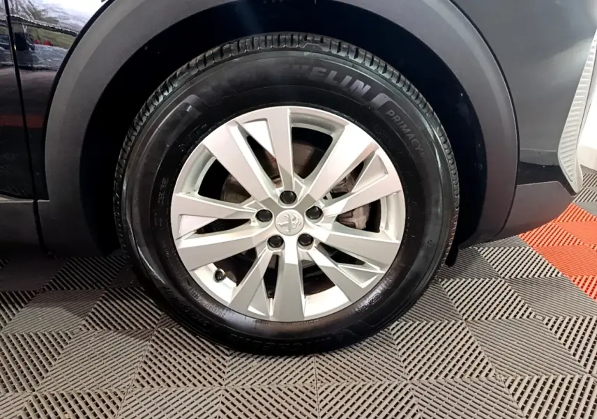 Gros plan sur la roue avant droite d’un Peugeot 3008 noir, mettant en valeur la jante alliage et le pneu Michelin.