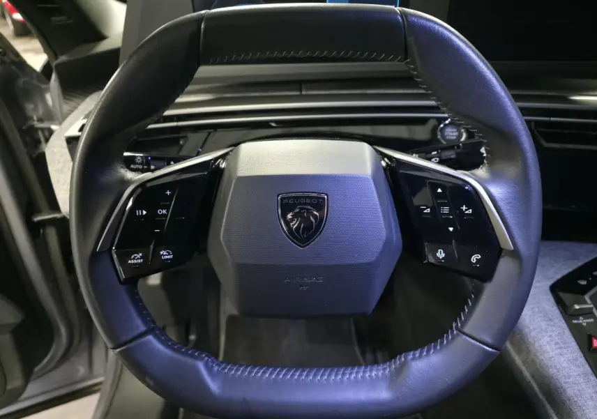 Volant compact en cuir noir avec logo Peugeot au centre, vue rapprochée de face dans un Peugeot 3008 gris 2025.