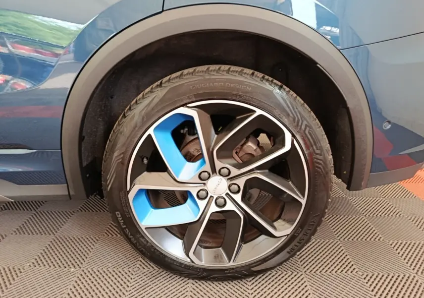 Gros plan sur la roue arrière droite d’un Link & Co 01 bleu avec jante bicolore noire et bleue design Giugiaro.