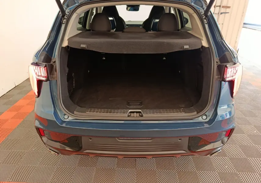 Vue arrière du coffre ouvert du SUV bleu LINK & CO 01 hybride rechargeable, intérieur spacieux et tapis noir visible.