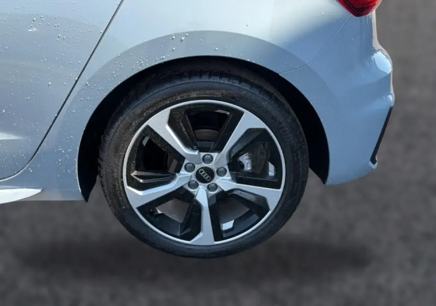 Gros plan sur la roue arrière droite d’une Audi A1 Sportback gris arrow avec jante alu bicolore et carrosserie mouillée.