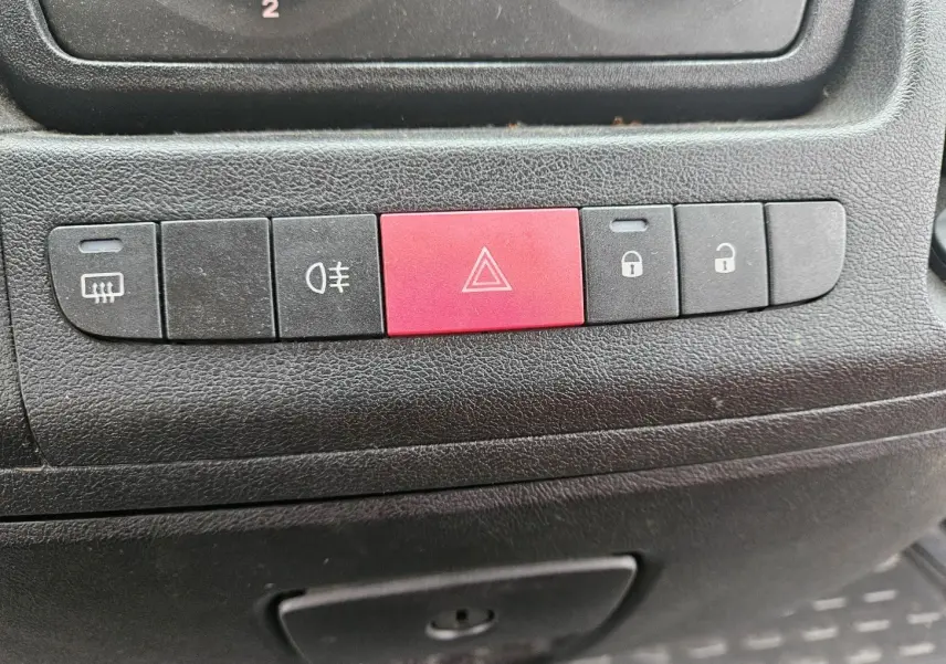 Gros plan sur les boutons de commande noirs et rouge du tableau de bord du Fiat Ducato Combi blanc 2014.