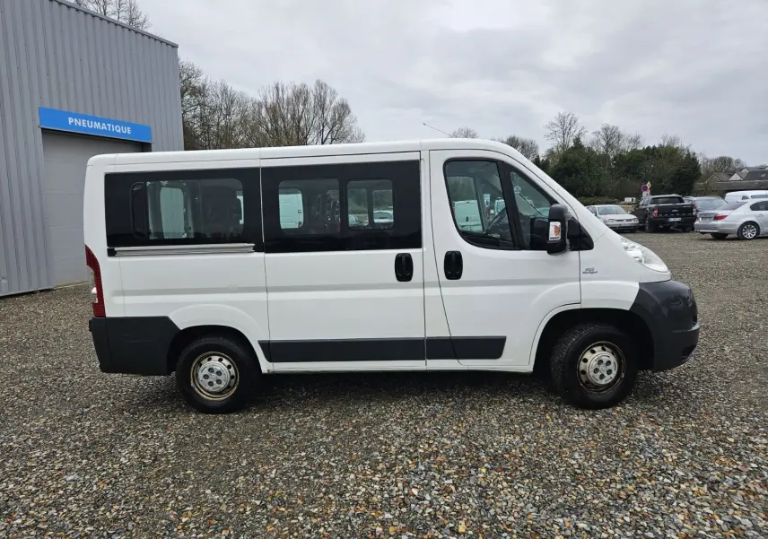 Profil côté gauche d'un FIAT Ducato Combi blanc 2014, fourgon 9 places avec fenêtres teintées et protections noires.