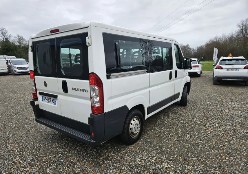 Fiat Ducato Combi blanc vu en 3/4 arrière droit, fourgon 9 places avec vitres latérales teintées et porte arrière double.