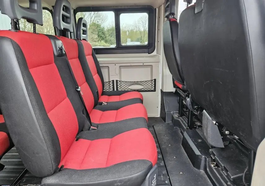 Vue intérieure latérale gauche du Fiat Ducato Combi 2014 blanc, sièges rouges et noirs pour 9 places.