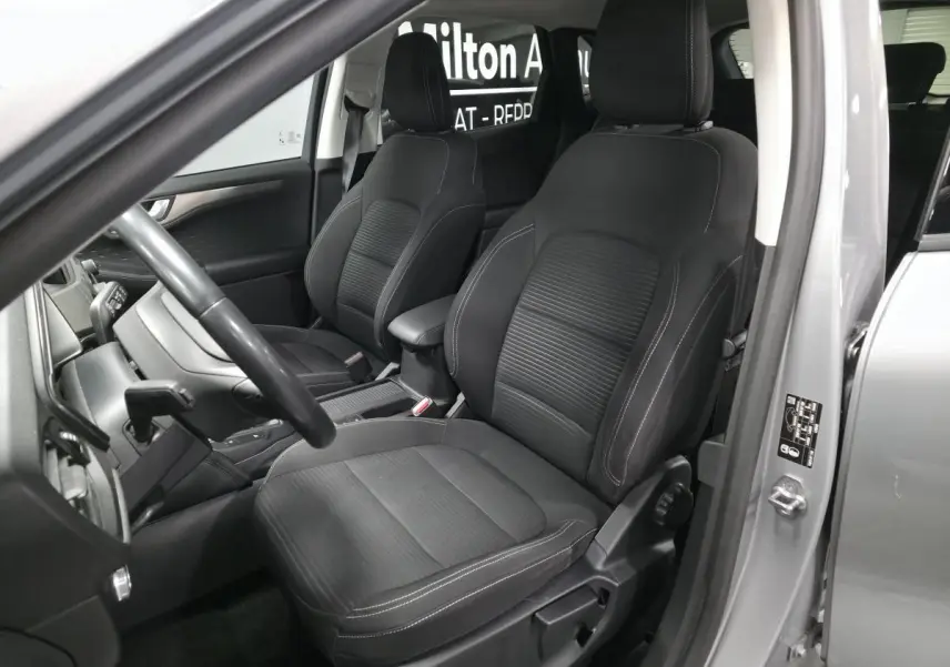 Vue intérieure côté conducteur du Ford Kuga gris 2021, sièges tissu noirs avec coutures blanches visibles.