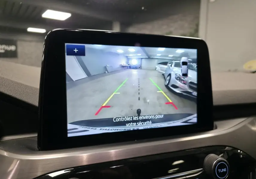 Écran central affichant la caméra de recul du Ford Kuga gris, avec guidage de trajectoire coloré et vue arrière intérieure.