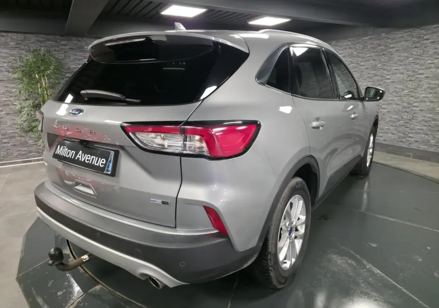 Vue 3/4 arrière droit d'un Ford Kuga gris métallisé avec crochet d'attelage et vitres arrière surteintées en intérieur showroom.