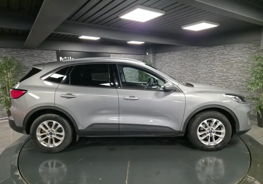 Profil côté gauche d'un Ford Kuga gris métallisé 2021 avec vitres arrière surteintées dans un showroom.