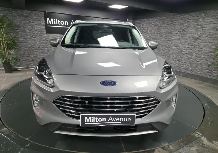 Vue frontale d'un Ford Kuga gris métallisé avec calandre chromée et phares LED dans un showroom.