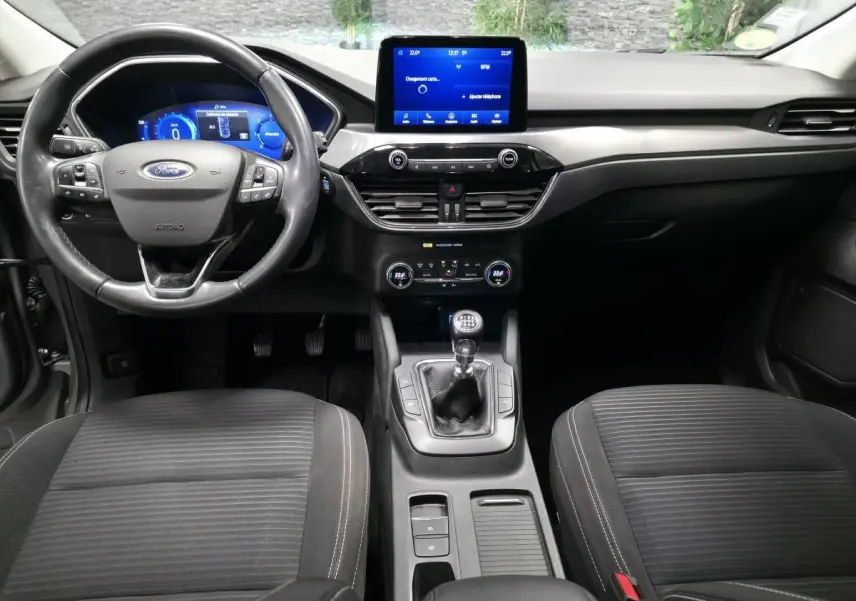 Vue intérieure frontale du Ford Kuga 2021 gris, avec volant 3 branches, écran tactile central et levier de vitesses manuel.